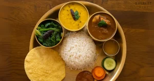 Traditional Nepali thali with rice, curry, lentils, greens, and papad.