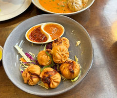 A plate of Nepalese fried momos with two dipping sauces, garnished with shredded lettuce.